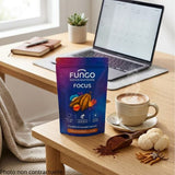 sachet posé sur un bureau moderne en chêne clair. À côté une belle tasse en céramique contient un riche et onctueux latte au cacao chaud. À côté de la tasse, de la poudre de cacao bio cru, un morceau frais de champignon crinière de lion et un petit champignon Cordyceps séché