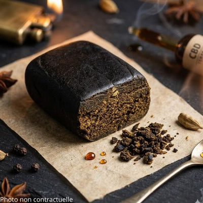 dark black CBD solid hash block (Afghan Hash style) resting on a piece of rustic parchment paper over a dark slate table